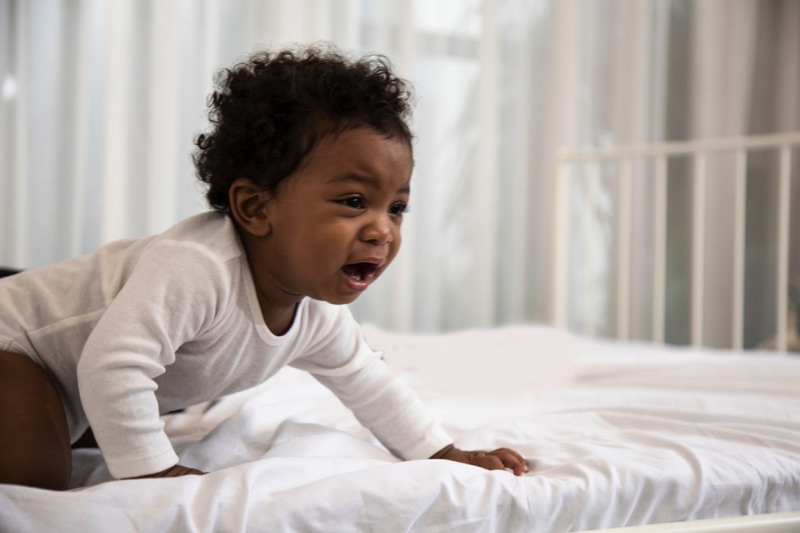 Baby crawling on bed and crying