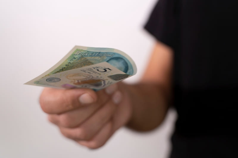 Hand offering child a £5 note